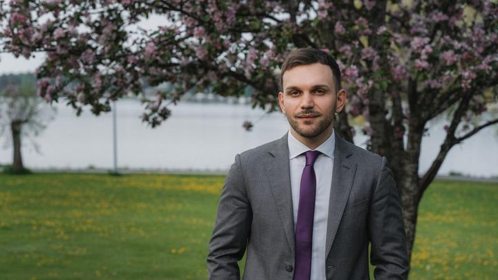 Davide Sandretto seisoo puku päällä meren rannalla, taustalla kukkiva puu.