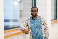 Emmanuel Anti seisoo ikkunan vieressä ja hymyilee. Hänellä on kuviollinen paita.