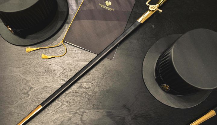 Kaksi mustaa tohtorinhattua ja akateeminen miekka pöydällä.