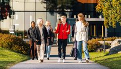 Ryhmä opiskelijoita kävelee yhdessä ulkona kampuksella aurinkoisena päivänä.