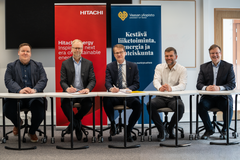 Kuvassa viisi henkilöä istuu pöydän ääressä, taustalla Hitachi Energyn ja Vaasan yliopiston bannereita.