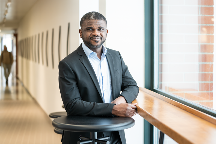 Akpojoto Siemuri seisoo käytävällä ja nojaa ikkunan edessä olevaan tasoon.