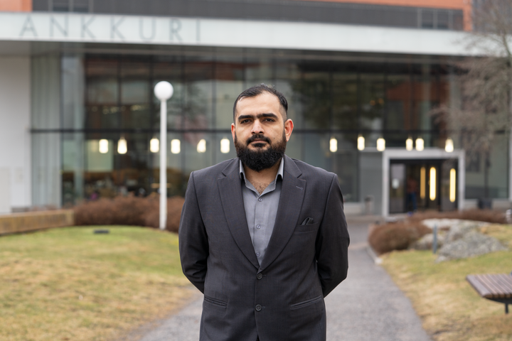Hussain Khan seisoo ulkona tummassa puvussa yliopiston rakennuksen edessä.