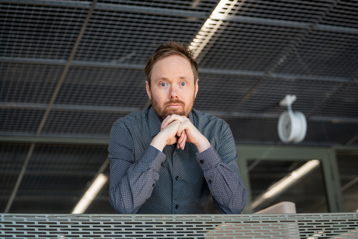 Jussi Tanskanen seisoo sisätiloissa, kädet ristissä kaiteen päällä.