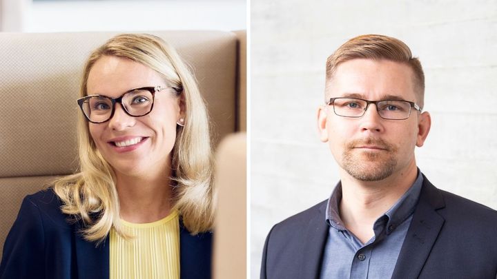 Kaksi henkilöä katsoo kameraan, taustalla neutraali sisustus.