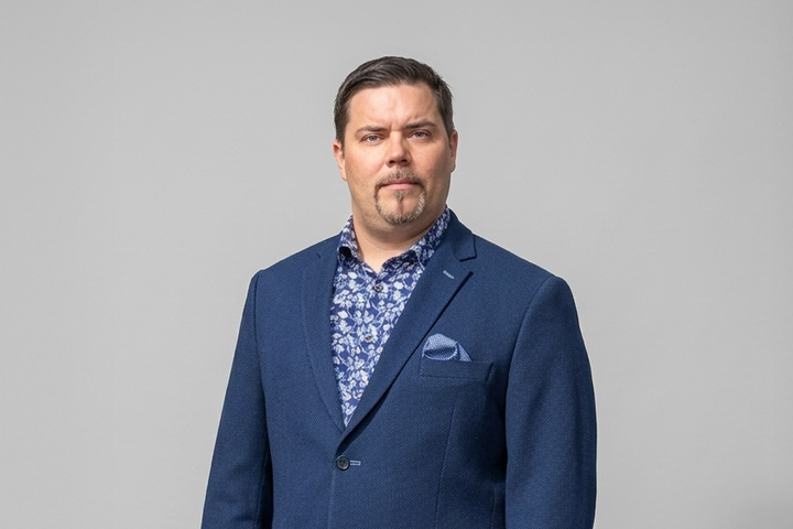 Pekka Suominen sinisessä puvussa harmaan taustan edessä.