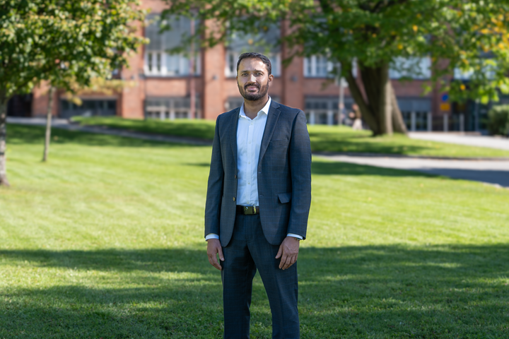 Arshed Iqbal seisomassa vehreällä nurmikolla. Taustalla näkyy tiilirakennus ja puita.