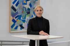 Marina Kinnunen seisoo valkoisen pöydän ääressä, taustalla on värikäs maalaus.