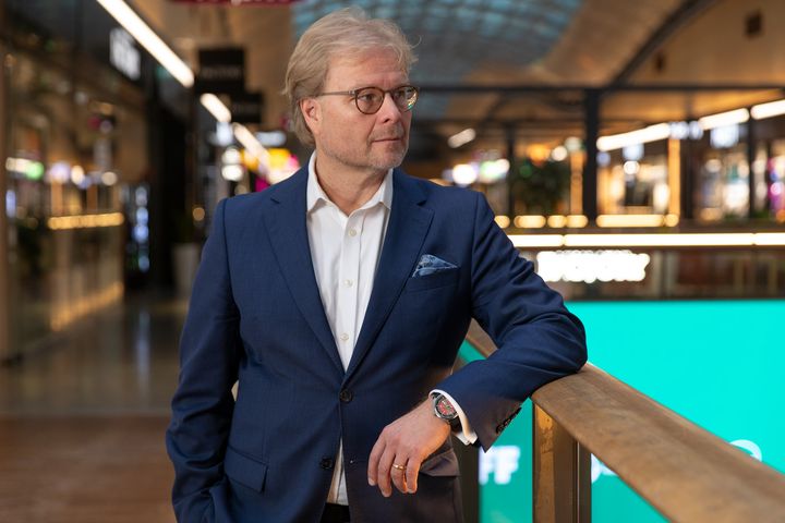Atte Palomäki sinisessä puvussa nojaa kaiteeseen kauppakeskuksessa.