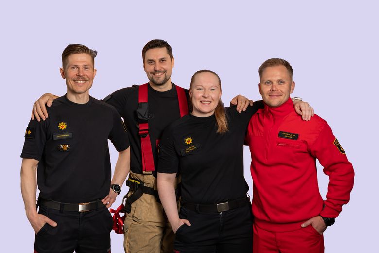 Neljä henkilöä seisovat kädet toistena olkapäillä ja katsovat hymyillen kameraan. Ensimmäisellä kolmella henkilöllä pelastustoimen virka-asu ja neljännellä ensihoitajan työasu.