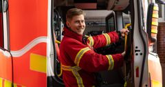 Pelastaja sammutushaalareissa katsoo kameraan ja on kiipeämässä paloautoon.