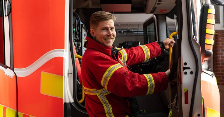 Pelastaja sammutushaalareissa katsoo kameraan ja on kiipeämässä paloautoon.