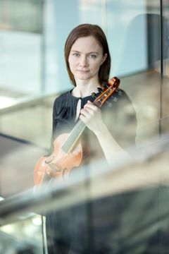 Kuvassa viulisti istuu ja katsoo kameraan.