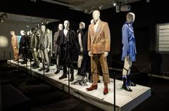 Useampi mallinukke pukeutuneena muodikkaisiin miesten juhlapukuihin, esillä näyttelytilassa.