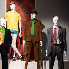 Näyttelytilassa seisoo kolme eri aikakauden miesten muodin mukaan puettua mallinukkea.