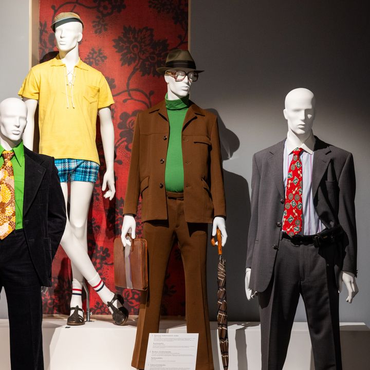 Näyttelytilassa seisoo kolme eri aikakauden miesten muodin mukaan puettua mallinukkea.