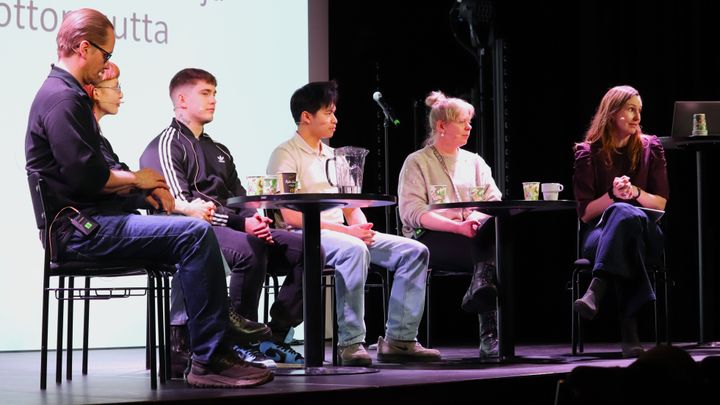 Henkilöitä istumassa tuoleilla lavalla