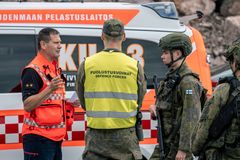 Oranssiin palomestariliiviin, keltaiseen Puolustusvoimien liiviin ja varusmiesvaatetukseen pukeutuneet miehet keskustelevat. Taustalla palomestarin auto.