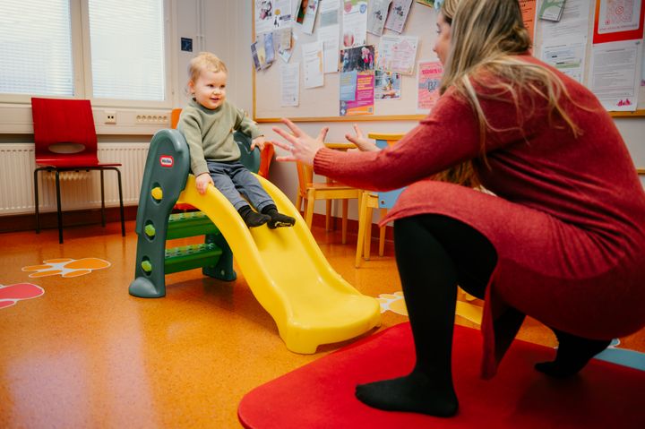 Lapsi laskee liukumäkeä, henkilö ottaa vastaan.