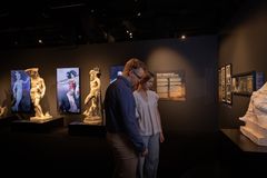 Pariskunta tutkii näyttelyesineitä museossa. Taustalla näkyy patsaita ja kuvia supersankareista antiikista nykypäivään.