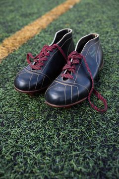 Vanha pari jalkapallokenkiä vihreällä kentällä.