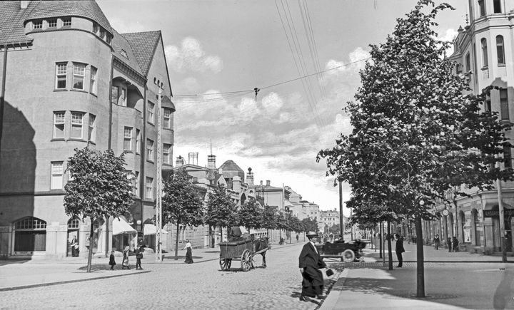 Raukean kesäinen alkuillan hetki Hämeenkadun ja Kuninkaankadun risteyksessä vuonna 1913. Kaupunkilaiset liikkuvat jalan, hevosella tai taksilla. Vasemmalla on Blomin talo ja oikealla Pulla-Helinin talo.