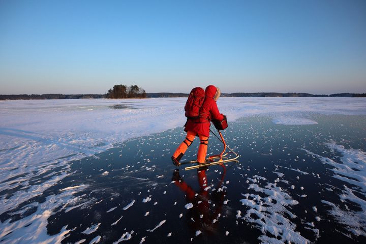 Kuvassa henkilö potkukelkkailee jäällä talvimaisemassa selässään punainen reppu.