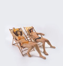 Veistos, jossa kaksi bikineissä olevaa naista istuu aurinkotuoleissa rinnakkain.