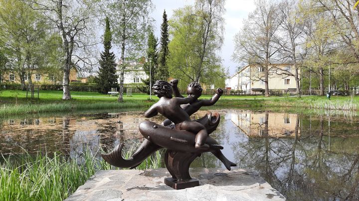 Kahta kaloilla ratsstavaa poikaa esittävä veistos lammen rannalla.