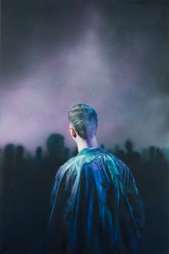 Nuori nahkatakkinen mies seisoo tehdassalissa, jossa reivit menossa.