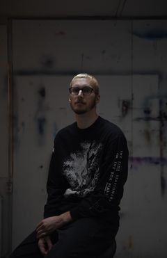 Hämärä valokuva nuoresta, pitkästä ja vaaleahiuksisesta miehestä.