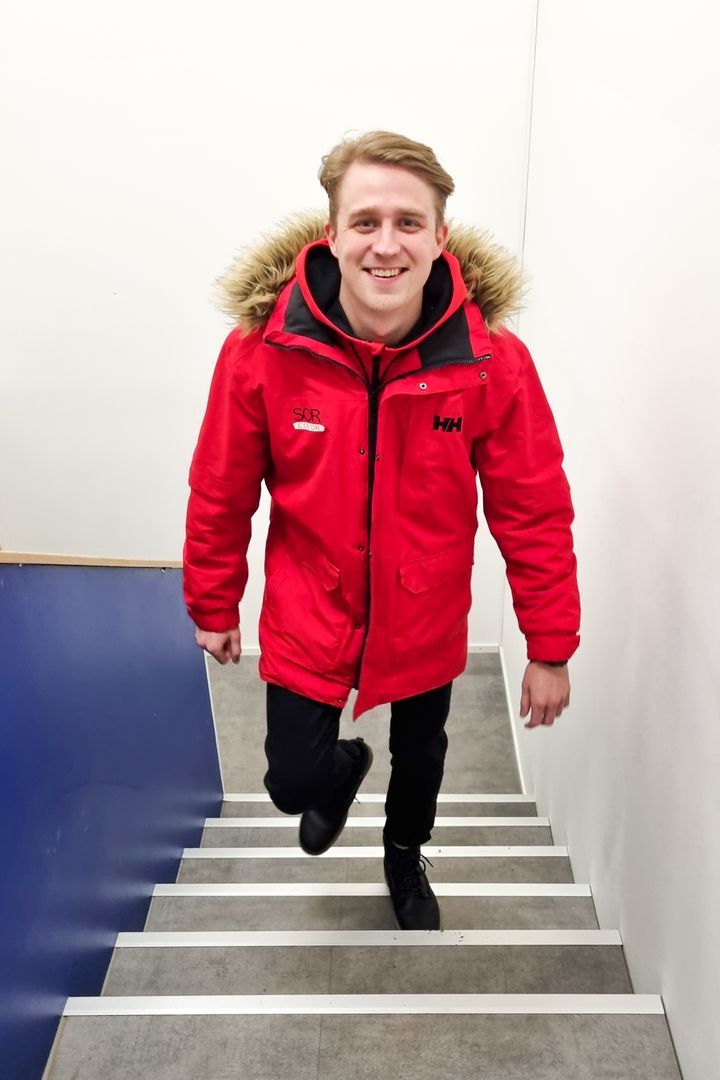 Mies kävelee hymyillen portaita ylös punainen takki yllään