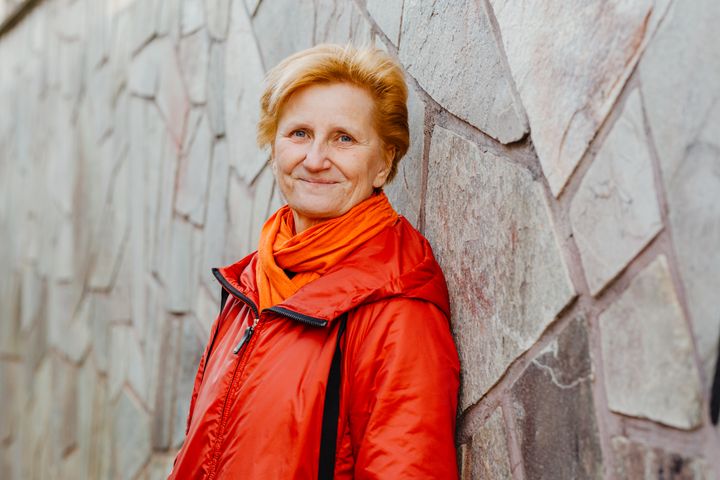 Nainen seisoo kivimuuria vasten ja hymyilee