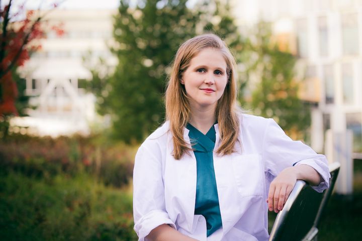 Reetta Vanhanen istuu ulkona penkillä lääkäritakki päällä.