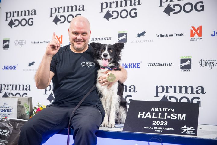 Jaakko Suoknuuti ja bordercollie Wow palkintopallilla hallisuomenmestaruuskultamitali kaulassa ja palkinnot vieressä.
