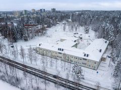 Talvinen koulurakennus lumisessa maisemassa, jota ympäröi puita ja tie.