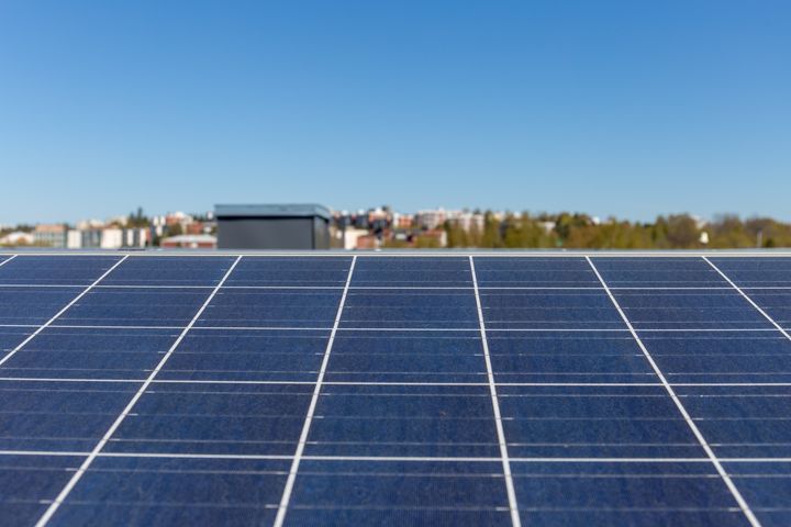 Aurinkosähköpaneeleita katolla. Kaupungin metsä ja taloja taustalla.