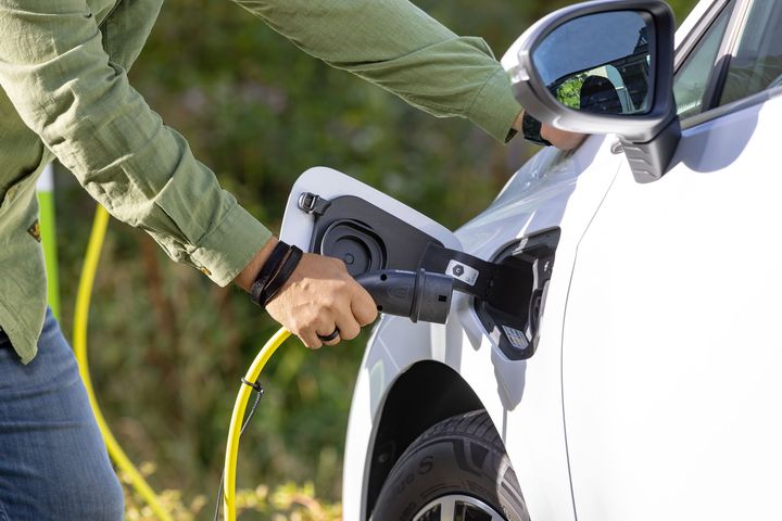 Henkilö, jolla on vihreä takki lataa valkoista sähköautoa.