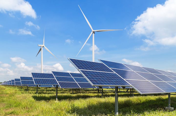 Solar panels and two wind turbines on a field, sky with couple of clouds.