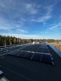 Aurinkopaneeleita rakennuksen katolla, taustalla metsää ja sininen taivas.