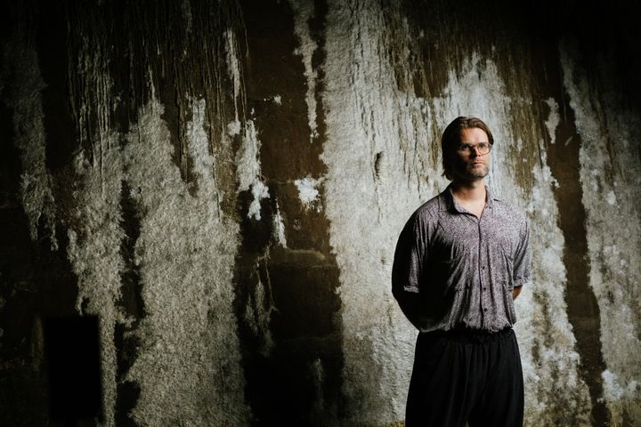 Jakob Kudsk Steensen standing against a textured, weathered wall with hands behind their back.