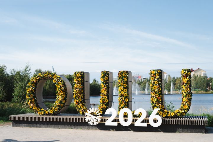 Oulun Ainolanpuistossa Oulu2026-kirjaimet, koristeltu kukilla. Taustalla suihkulähteitä ja rakennuksia.