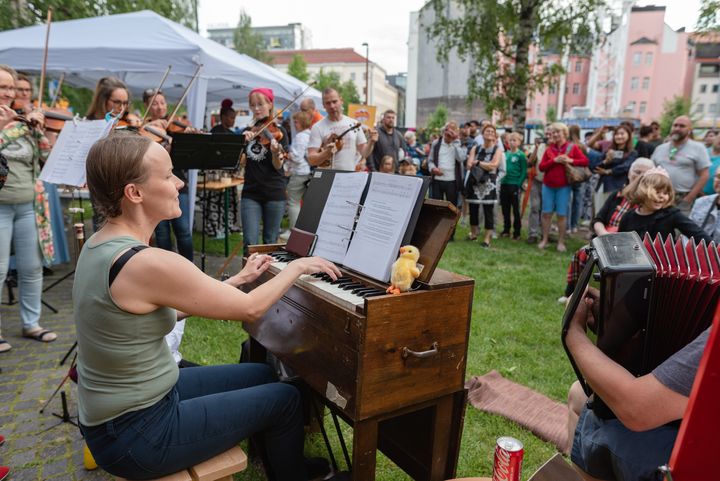 Esiintymässä Orivesi All Stars -pelimannikollektiivi ulkona Oulun keskustassa, ympärillä monenikäinen yleisö nauttii esityksestä.
