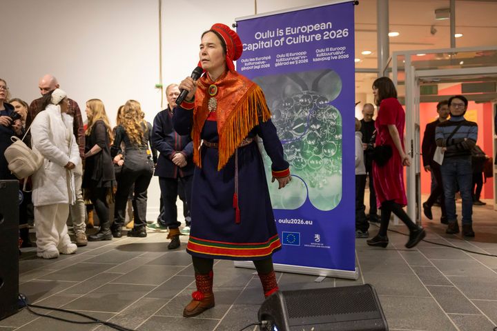 Nainen esiintyy perinteisessä asussa mikrofonin kanssa Oulun taidemuseolla.