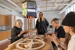 Kuva esittää neljää henkilöä työskentelemässä suurten puisten rattaiden parissa työpajassa.