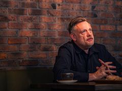 Kuvassa Andrew Melchior tiiliseinän edustalla istumassa mietteliäänä.