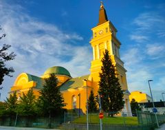Oulu Cathedral with a bright yellow facade and green roof under a blue sky.