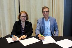 Marjo Kaartinen och Tarmo Martikainen sitter vid ett bord och undertecknar avtalsdokument.