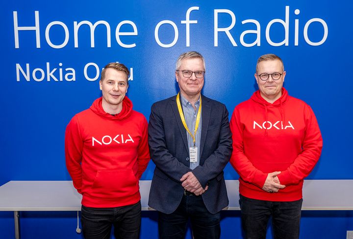 Koristeellinen kuva, jossa kuvattuna Nokian tiloissa sinistä seinää vasten OSAOn kuntayhtymäjohtaja-rehtori Jarmo Paloniemi (keskellä) sekä Nokia Oulun tehtaanjohtaja Mikko Nissi (vasemmalla) ja Nokia Oulun yksikönjohtaja Jarkko Pyykkönen (oikealla).