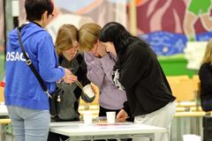 Kolme kilpailijaa siirtää makeisia syömäpuikoilla toiseen astiaan. Tuomari seuraa suoritusta.